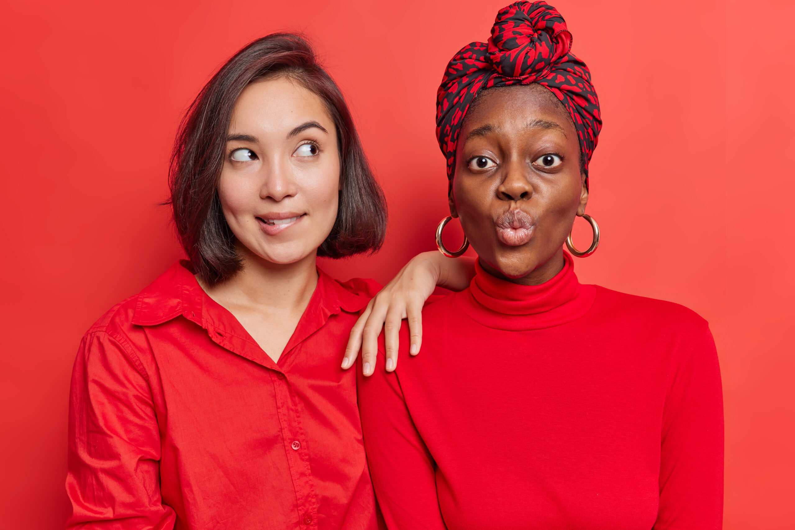 due ragazze di etnie diverse posano con facce buffe su uno sfondo rosso