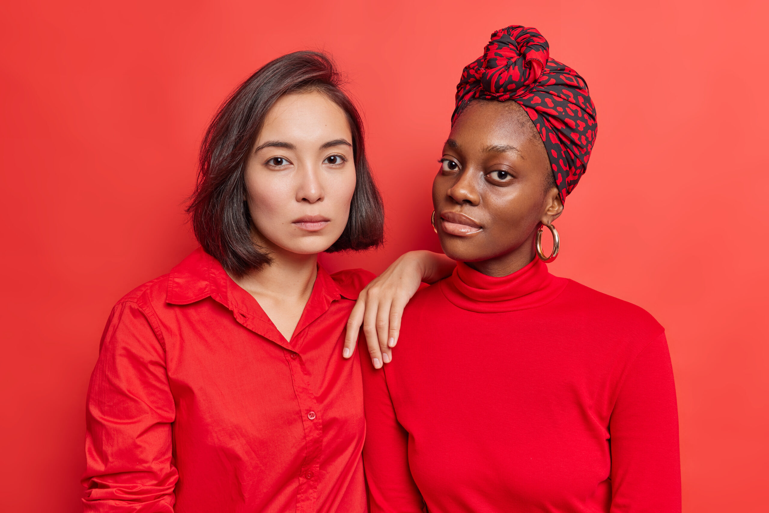 due ragazze di etnie diverse posano serie su uno sfondo rosso