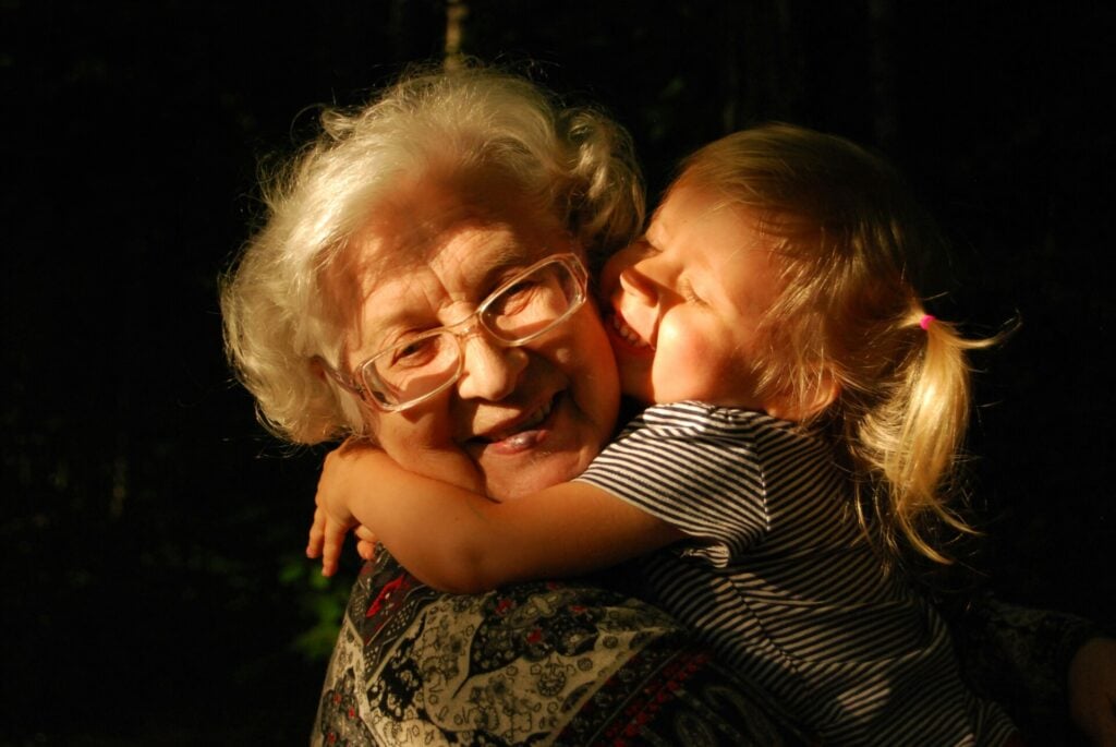 Nonni e nipoti, un legame unico di educazione e amore. Una nonna sorridente tiene tra le braccia la sua piccola nipotina che le tiene le braccia al collo