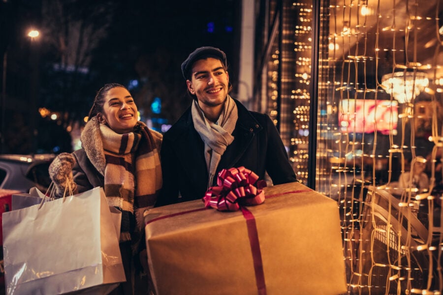 Vendere online. giovane uomo e giovane donna sorridenti che fanno shopping natalizio nei punti vendita della loro città