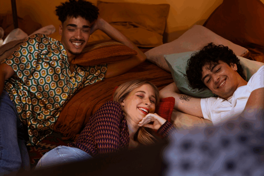 relazioni monogame e coppia aperta: tre ragazzi sorridenti sdraiati sul letto