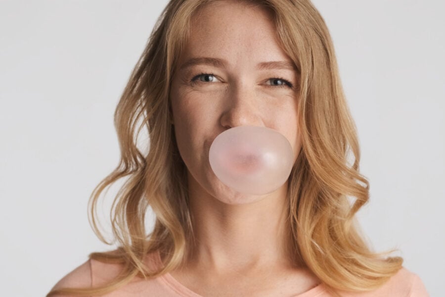 Masticare chewing gum: ragazza bionda che soffia divertita per fare una bolla con la gomma da masticare